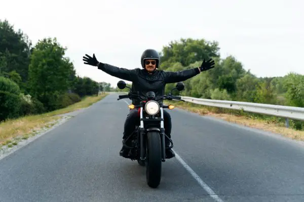 Motard bras écartés sur une route de campagne, la liberté du voyage à moto