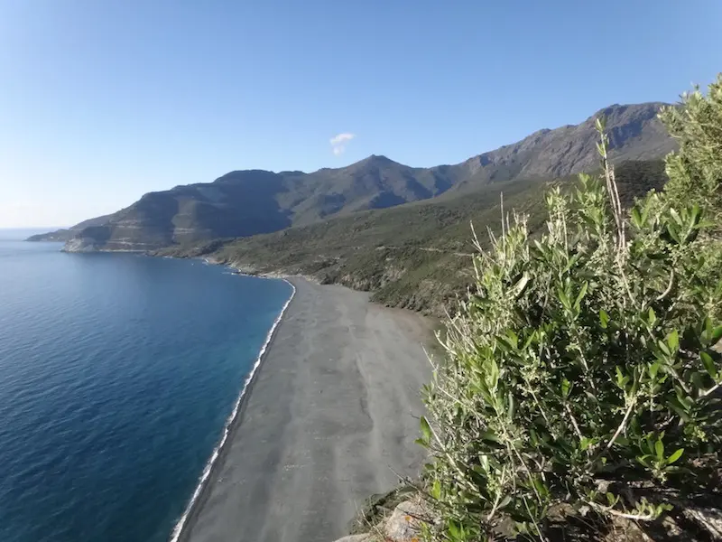 Plage de galets sombres au pied des montagnes du Cap Corse