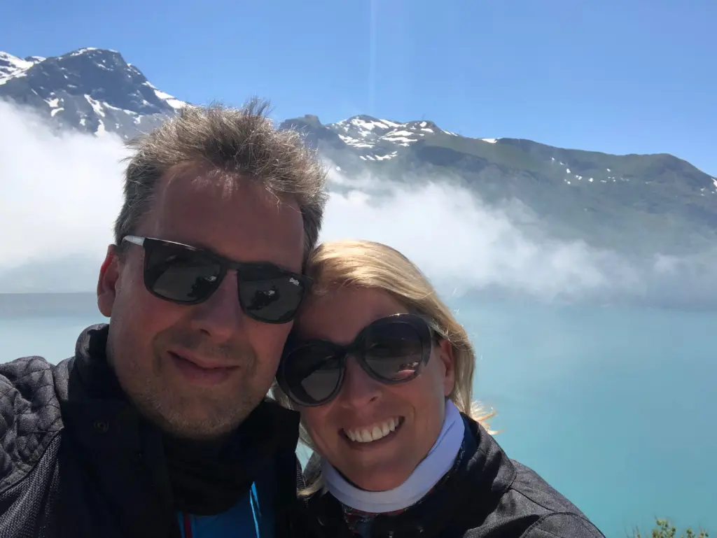 Deux voyageurs à moto devant un lac turquoise et des sommets enneigés
