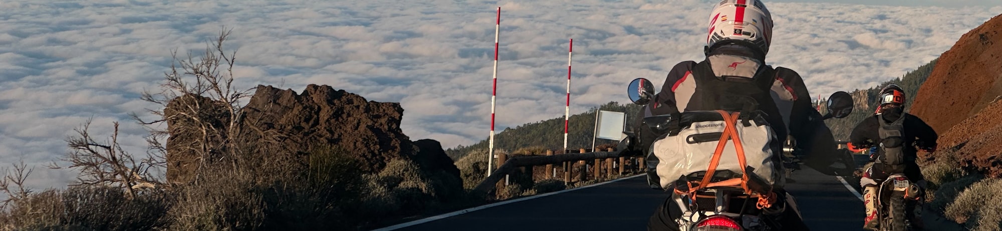 Deux motards sur une route de montagne au-dessus d'une mer de nuages