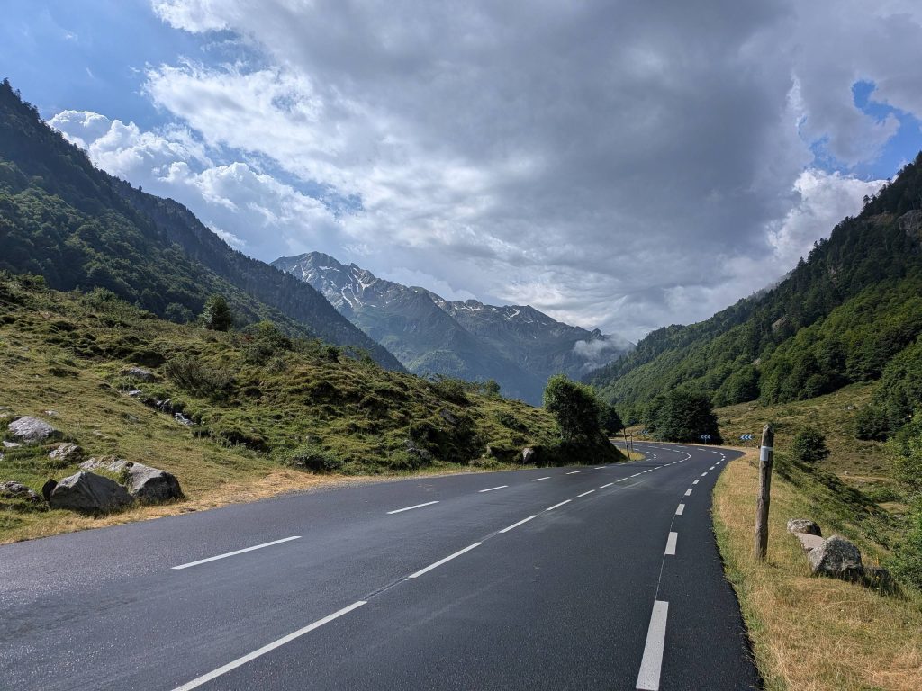 Route de montagne serpentant dans une vallée des Pyrénées, sommets enneigés en arrière-plan