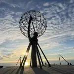 Le globe du Cap Nord se découpe sur le soleil de minuit, au bord du plateau, en voyage moto accompagné